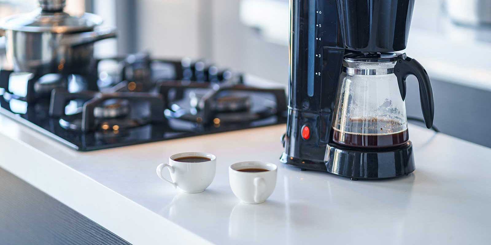 Two cups of coffee next to a drip coffee machine