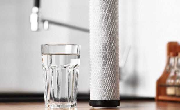 glass of clean fresh water and carbon filter cartridge on wooden table in a kitchen interior