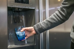 male hand is pouring cold water and ice cubes from dispenser of home fridge