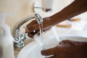 cropped hands of man filling water in glass at sink
