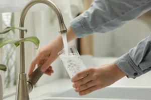 woman filling glass with water from tap at home, closeup
