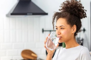 beautiful young afro american woman drinking clean water standing at home in the kitchen