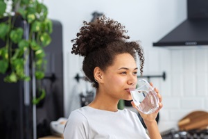 beautiful young Afro American woman drinking clean water standing at home in the kitchen