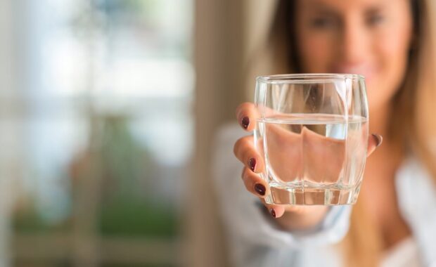 beautiful young woman smiling while holding a glass of water at home