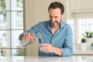 middle age man drinking a glass of water with a happy face standing and smiling with a confident smile showing teeth